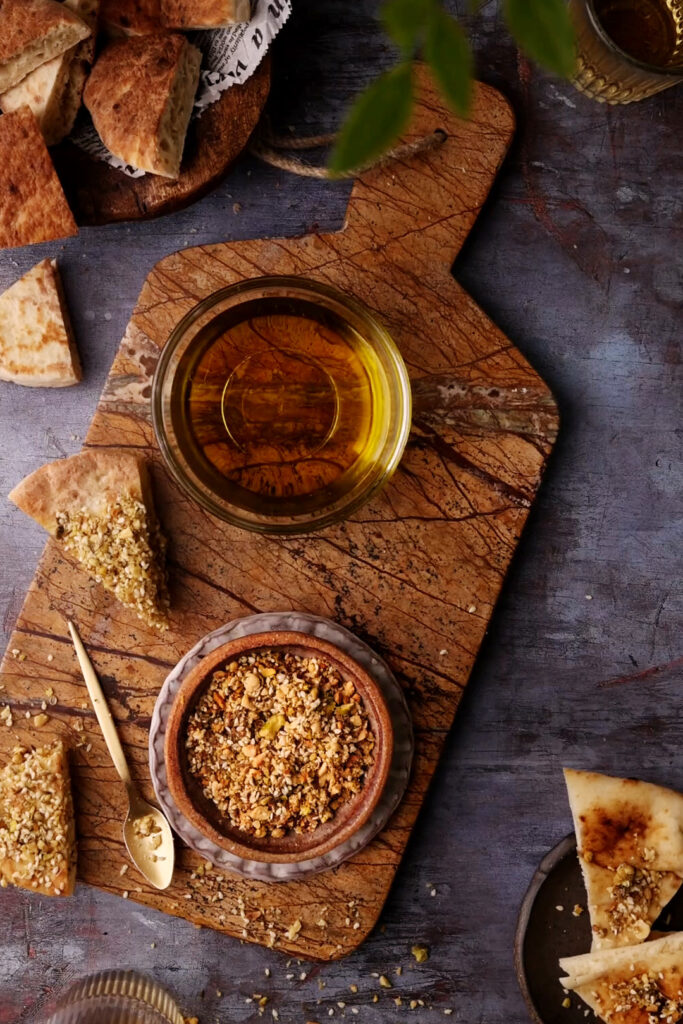 Bowl of homemade dukkah made with toasted nuts, sesame seeds, and spices, set beside olive oil and warm pita ready for dipping