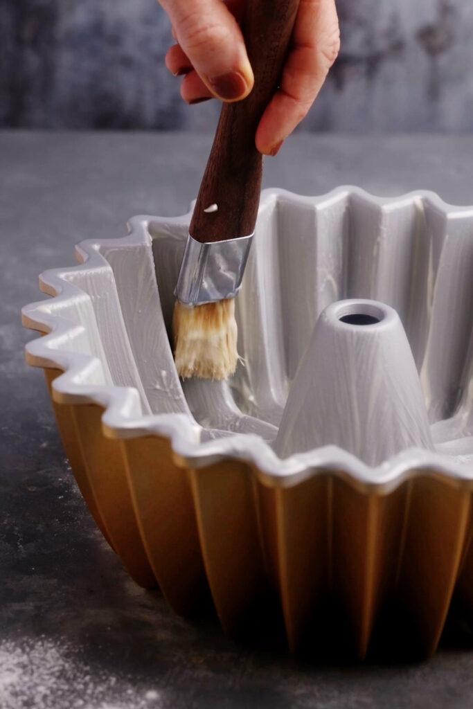 Brushing homemade cake release mixture into a fluted Bundt pan to ensure the Brown Butter Banana Bundt Cake releases cleanly after baking.