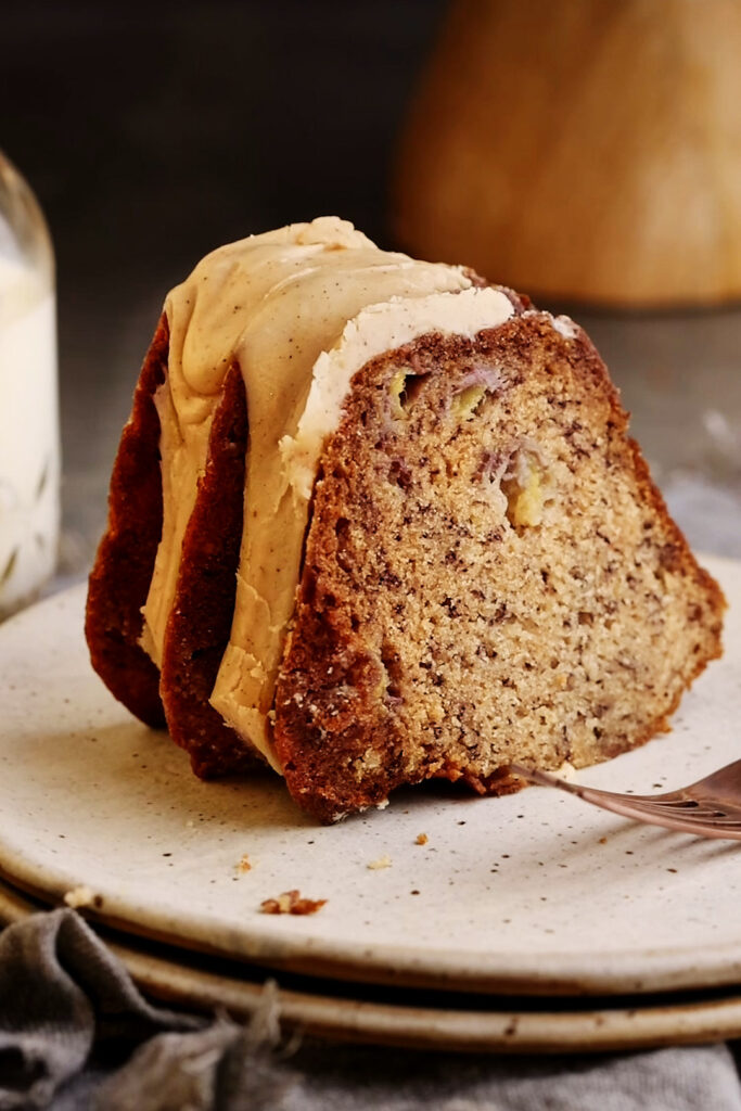 Slice of Brown Butter Banana Bundt Cake topped with maple glaze, revealing a soft, moist interior.
