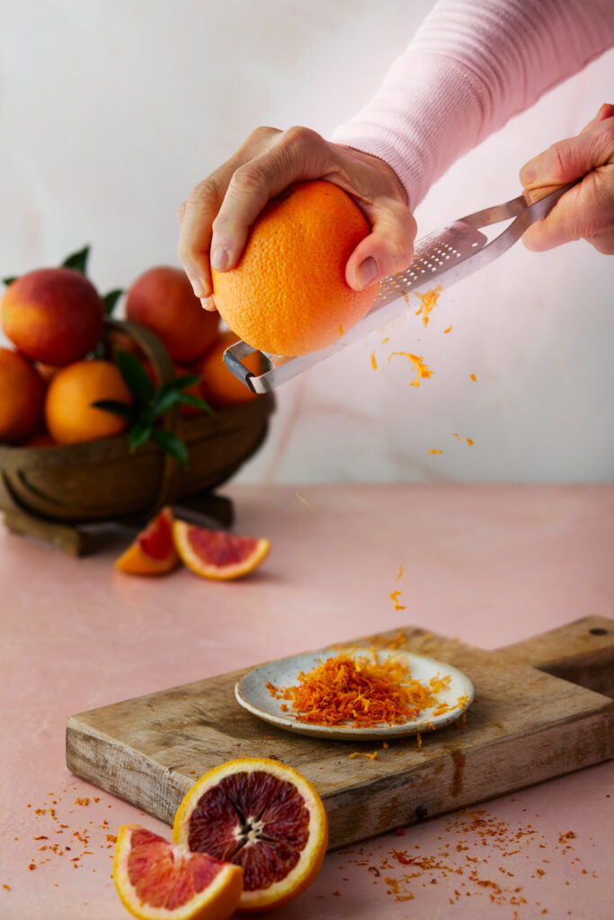 Blood orange being zested over a cutting board to add citrus flavour to Blood Orange Coconut Bundt Cake.