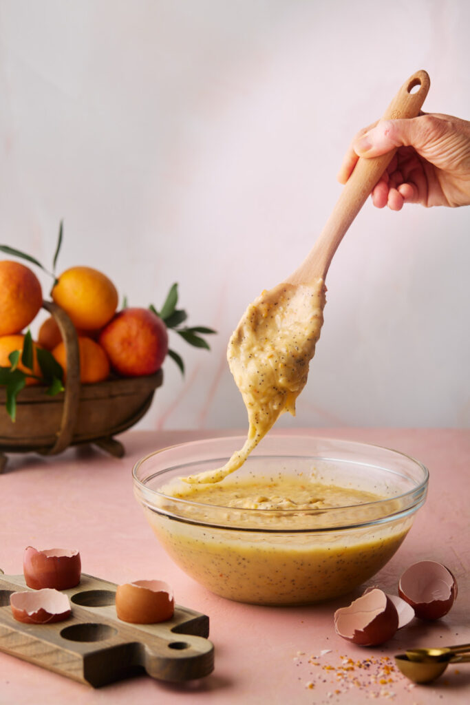 Thick Blood Orange Coconut cake batter with poppy seeds being lifted from a mixing bowl.