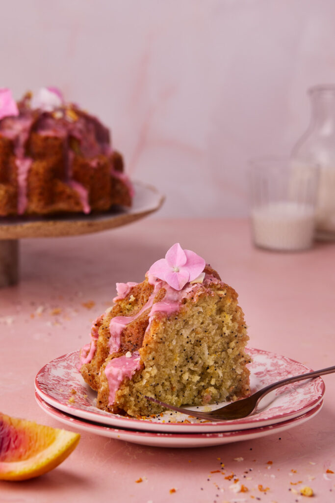 Slice of Blood Orange Coconut Bundt Cake with poppy seeds and pink blood orange glaze served on a vintage pink plate.