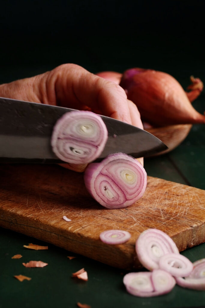 Close-up of shallots being sliced into thin rounds on a wooden cutting board for homemade pickled shallots