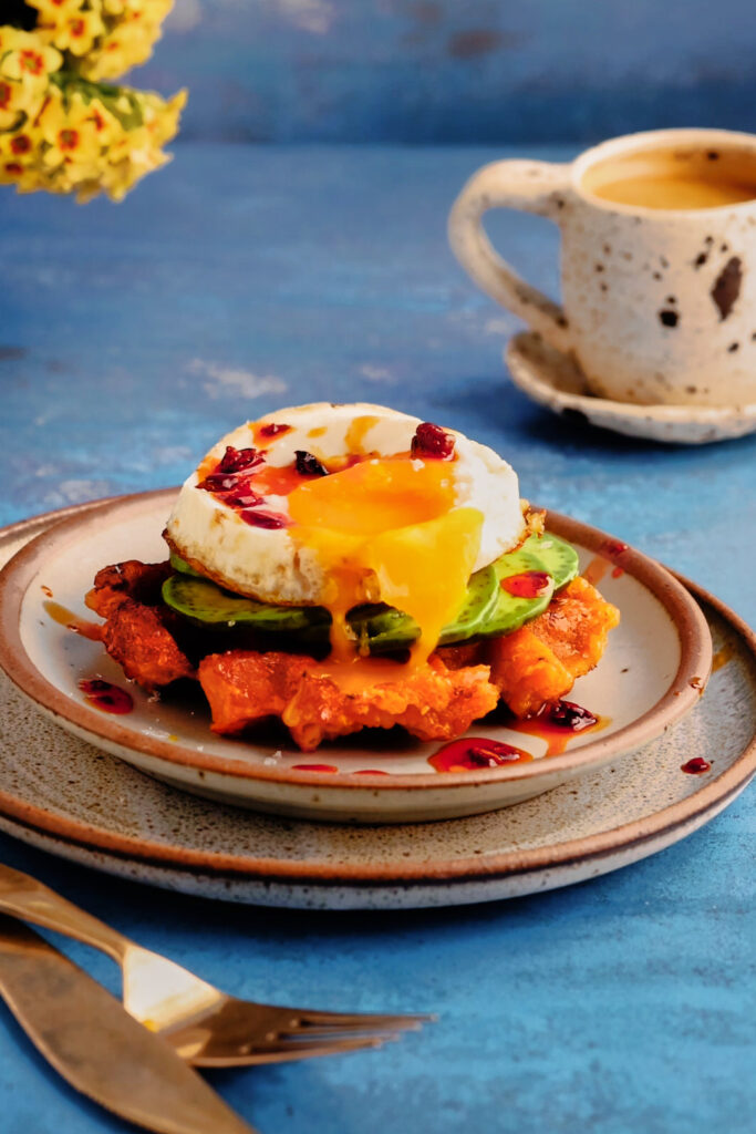 Crispy sweet potato breakfast waffle topped with avocado, fried egg, and chile crisp for a high-protein, high-fibre breakfast.